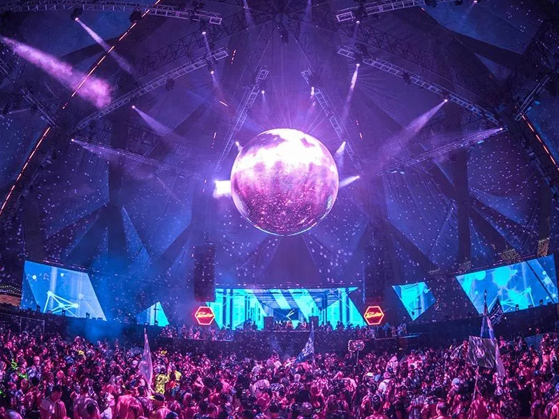 A large spherical LED screen hangs overhead, glowing vividly, while a dense crowd below immerses themselves in the captivating, immersive atmosphere of the event.
