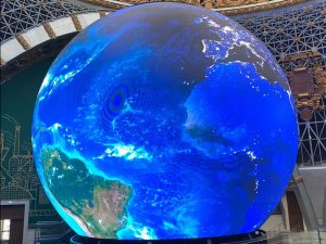 a large, spherical LED display screen designed to resemble the Earth. It vividly presents a detailed view of the planet’s oceans, landmasses